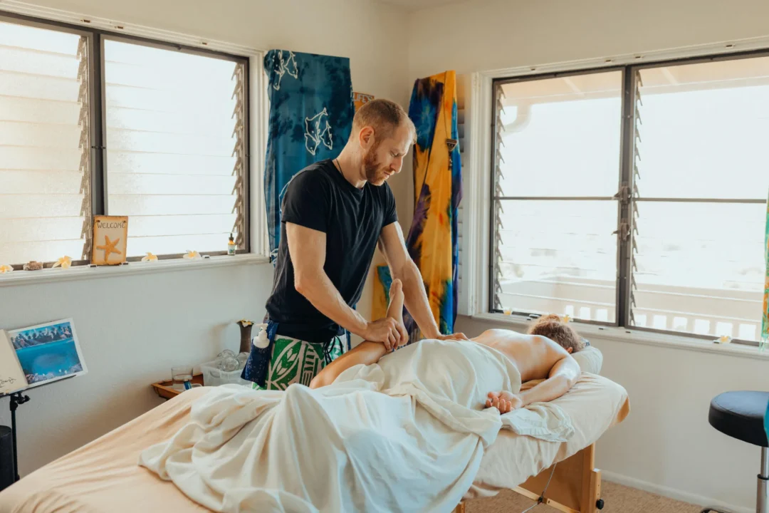 A massage therapist works on a client's back in a serene room with large windows and colorful decor.